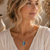 Woman wearing an Abalone Shell Oval Pendant on a delicate silver chain with a soft cream linen blouse. 🌿