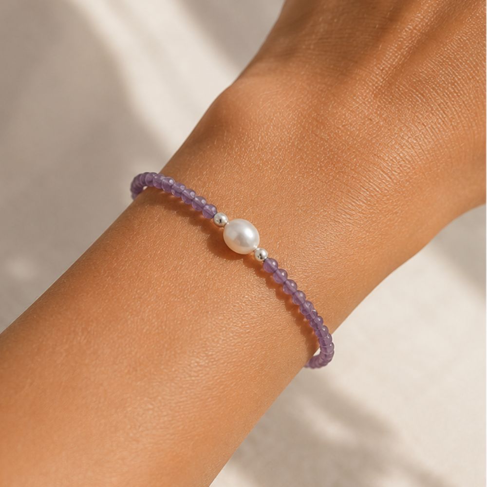 Purple beaded bracelet with a pearl on a wrist against a neutral background