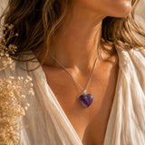 Woman wearing a necklace with a purple heart pendant, surrounded by dried flowers.