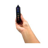 Hand holding a black crystal with chakra symbols on a white background