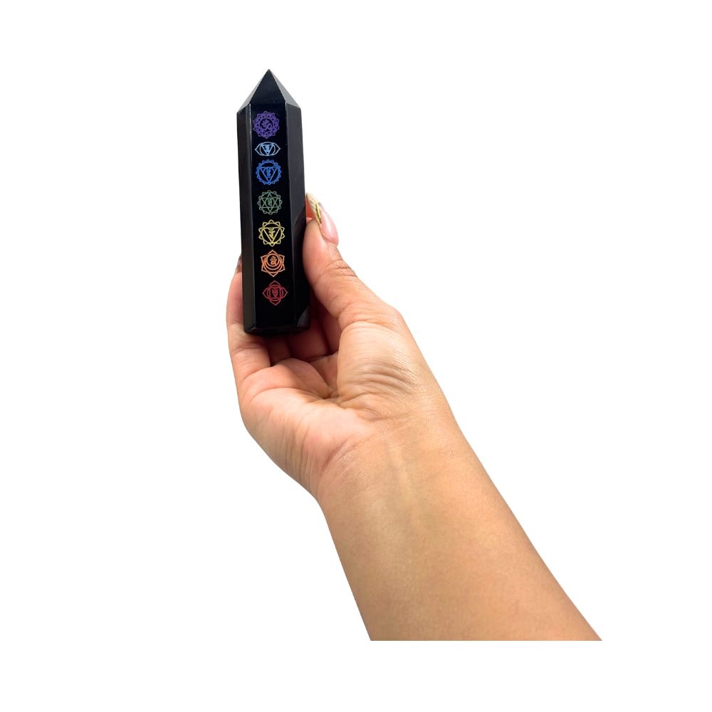 Hand holding a black crystal with chakra symbols on a white background
