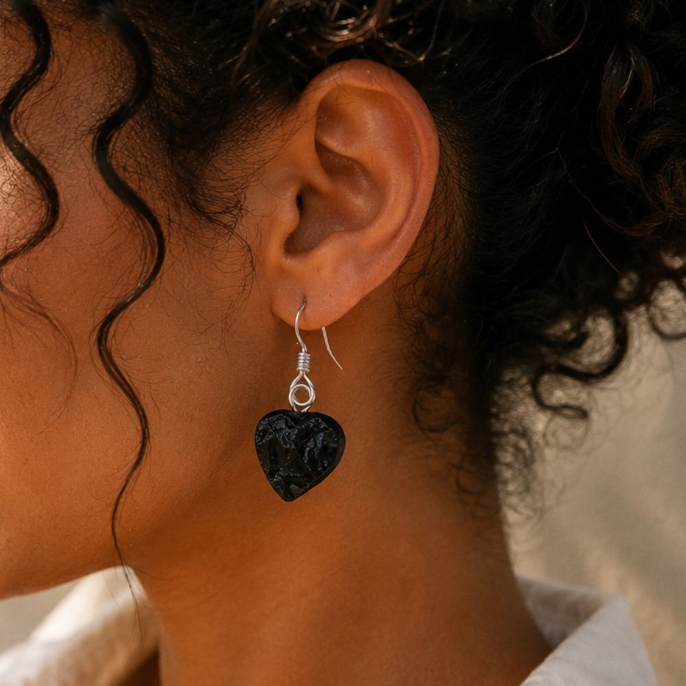 Close-up of an ear wearing a black heart-shaped earring with a blurred background