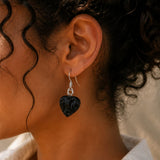 Close-up of an ear wearing a black heart-shaped earring with a blurred background