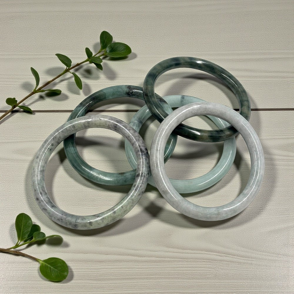 jade bracelets on a light wooden surface with green leaves.