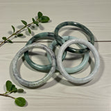 jade bracelets on a light wooden surface with green leaves.