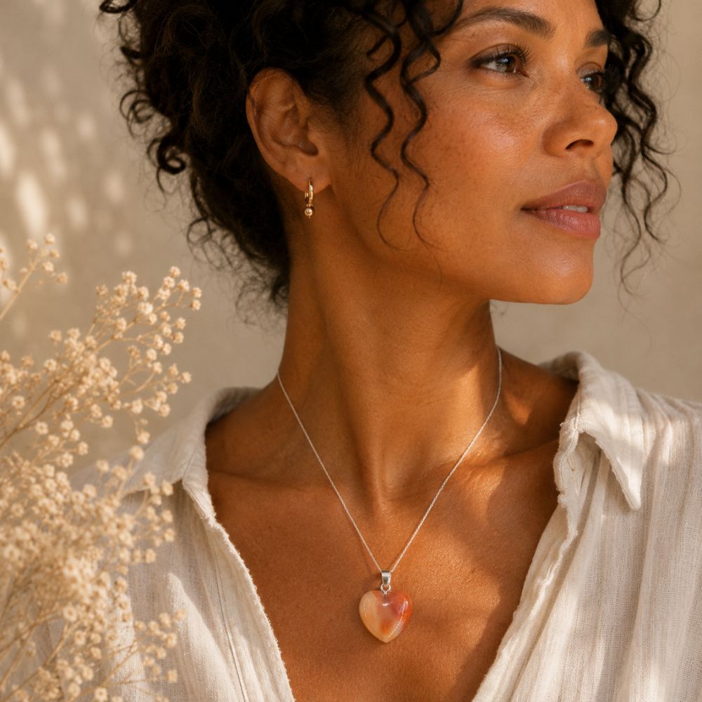 Woman wearing a necklace with a heart-shaped pendant, standing against a neutral background.