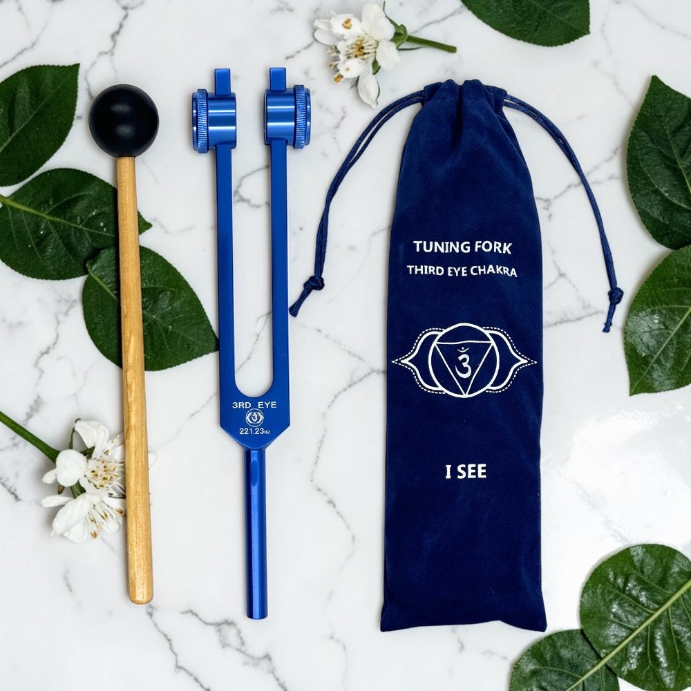 Blue tuning fork with wooden handle and blue pouch on a marble surface with leaves and flowers.