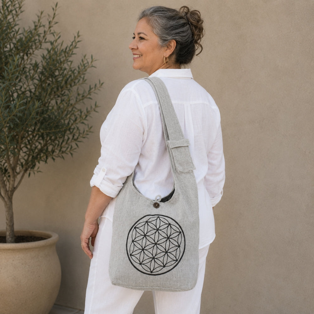 Woman wearing a gray tote bag with a geometric design, standing against a beige wall.