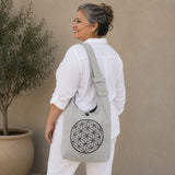 Woman wearing a gray tote bag with a geometric design, standing against a beige wall.