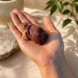 A small carved turtle figurine with a reddish-brown shell and pale head, resting on an open human hand in warm natural light.