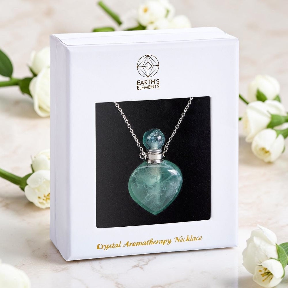 Crystal aromatherapy necklace in a white box with 'Earth's Elements' branding, surrounded by white flowers.