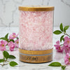 Pink Himalayan salt lamp with wooden base on a marble surface with pink flowers.