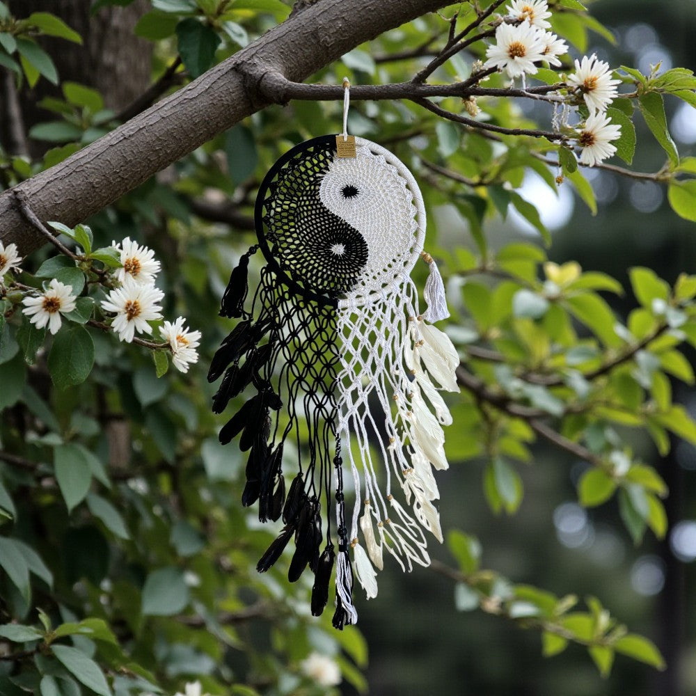 Dreamcatcher with yin yang symbol hanging from a tree branch with flowers.