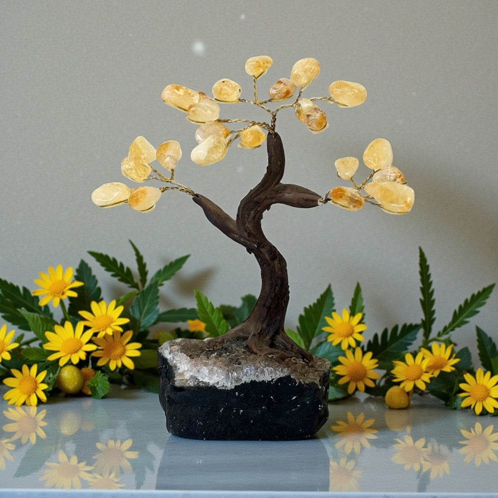 Decorative crystal tree with citrinestones on a reflective surface with flowers in the background