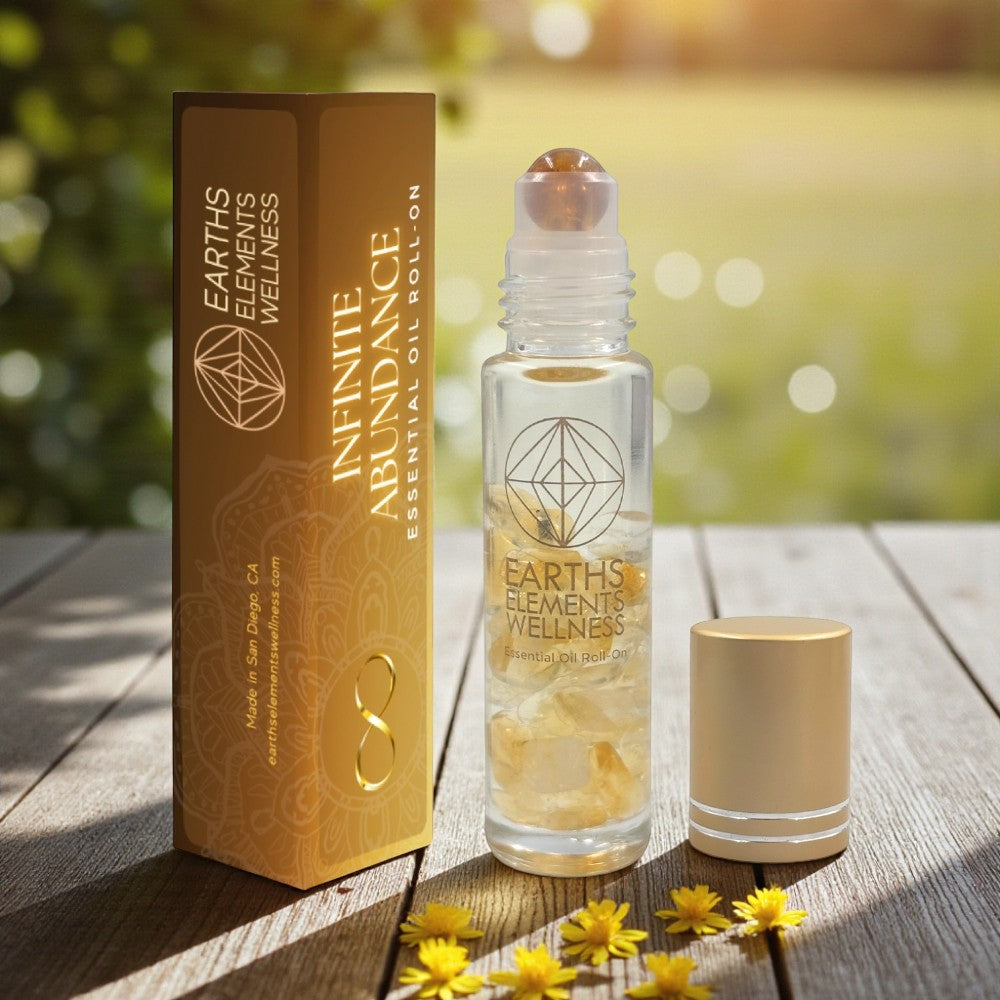 Earth's Elements Wellness Infinite Abundance essential oil roll-on bottle and packaging on a wooden surface with flowers.