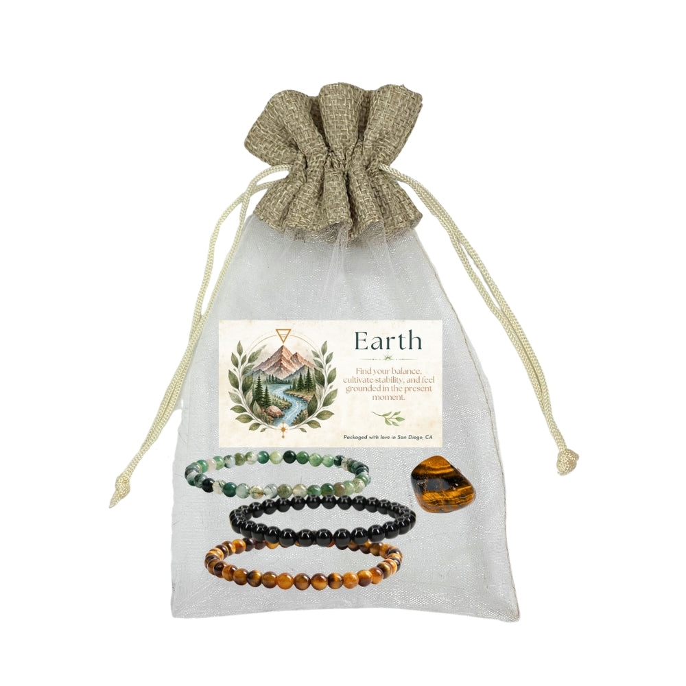 A gift set of four beaded bracelets and a polished stone displayed on a sheer white drawstring pouch with a printed label reading 'Earth'. The bracelets are made of moss agate, black obsidian, and tiger's eye with a tiger's eye tumble.