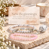 Three beaded stretch bracelets displayed on a stone slab with a branded card reading 'New Beginnings' and 'Earth's Gemstones.' The bracelets include howlite, labradorite, and rose quartz.
