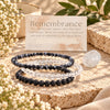 Three beaded stretch bracelets displayed on a textured stone slab with white flowers and green leaves. The bracelets are black lava stone, clear quartz, and snowflake obsidian.