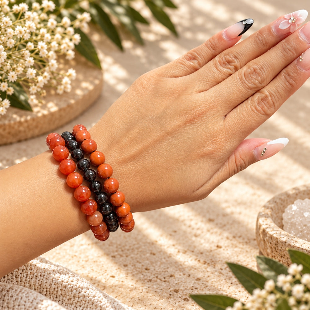 A close-up of a person's hand and wrist wearing three beaded bracelets. The bracelets are Carnelian, Garnet, and Red Jasper