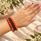 A close-up of a person's hand and wrist wearing three beaded bracelets. The bracelets are Carnelian, Garnet, and Red Jasper