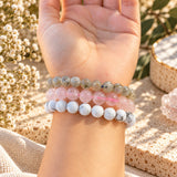 Three beaded stretch bracelets worn on a person's wrist, featuring howlite, labradorite, and rose quartz, displayed against a warm, boho-style background with dried flowers.