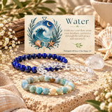 Three beaded bracelets arranged on sand with shells and dried flowers: blue lapis lazuli bracelet, an Amazonite and clear quartz bracelet. A printed card behind them reads “Water” with ocean artwork and small text about being packaged with love in San Diego, CA.
