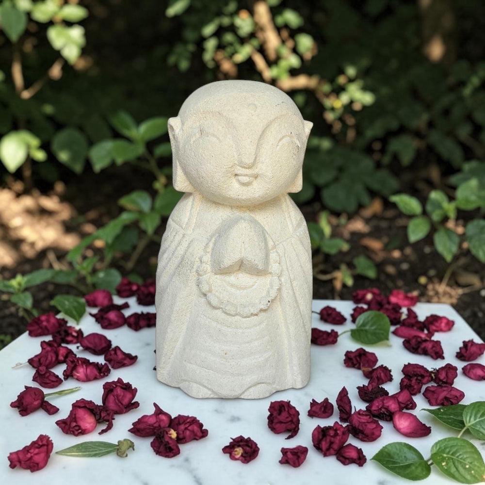 White stone statue of a seated figure with dried red flowers and green leaves on a marble surface.