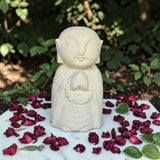 White stone statue of a seated figure with dried red flowers and green leaves on a marble surface.