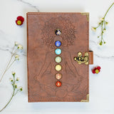 Brown leather journal with chakra design on a marble surface with flowers.