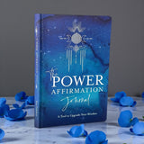 Blue journal titled 'The Power Affirmation Journal' with decorative elements on a gray background.