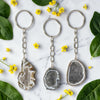 Three geode keychains on a marble surface with green leaves and yellow flowers.