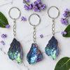 Three aura keychains on a marble surface with purple flowers and green leaves.