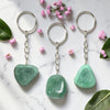 Three Green Aventurine keychains on a marble surface with pink flowers and leaves.