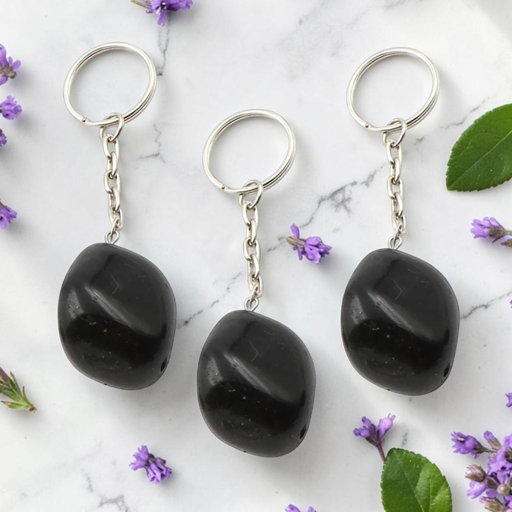 Three Black Obsidian keychains on a marble surface with purple flowers and green leaves.