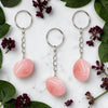 Three Rose Quartz keychains on a marble surface with green leaves and purple flowers.