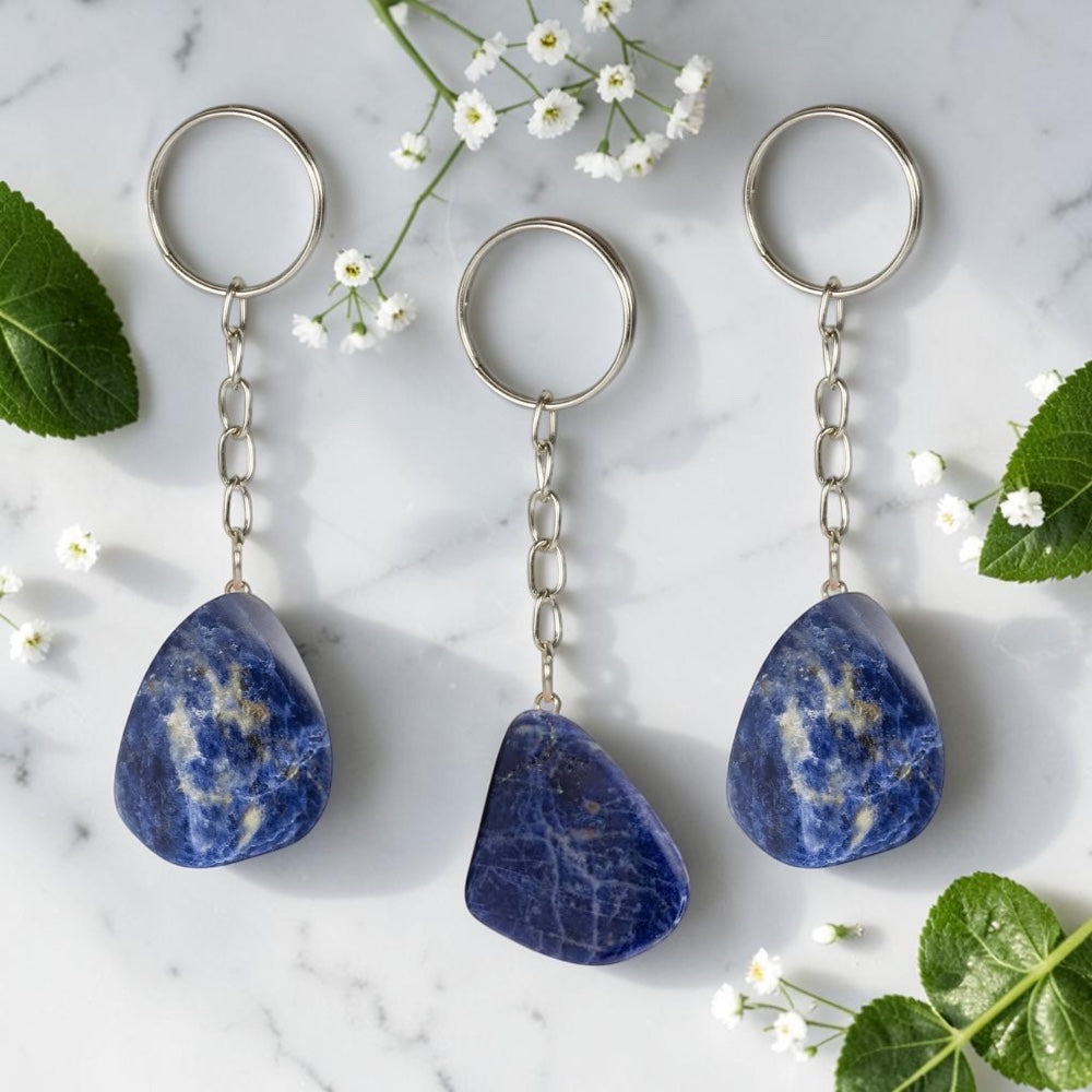 Three Sodalite keychains on a marble surface with flowers and leaves.
