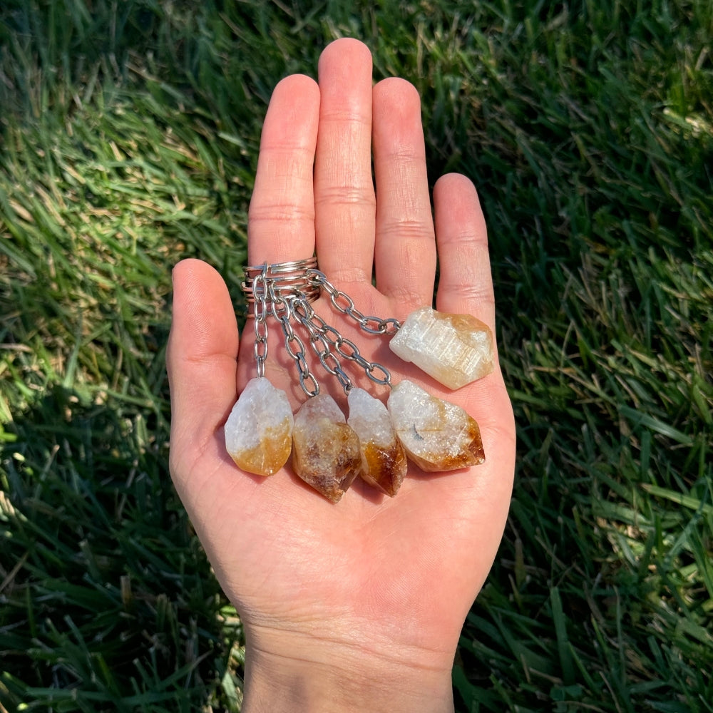 Hand holding citrine keychains against a grassy background