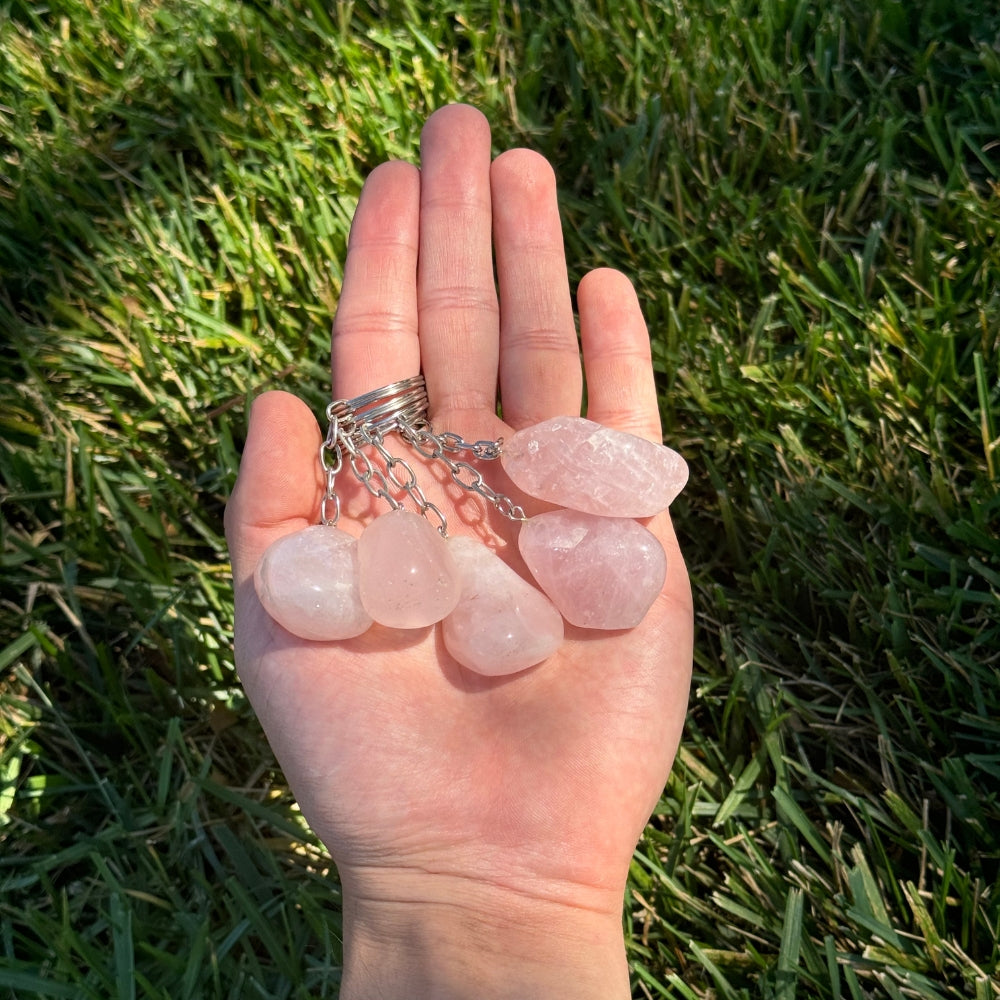 Hand holding a set of rose quartz keychains against a grass background