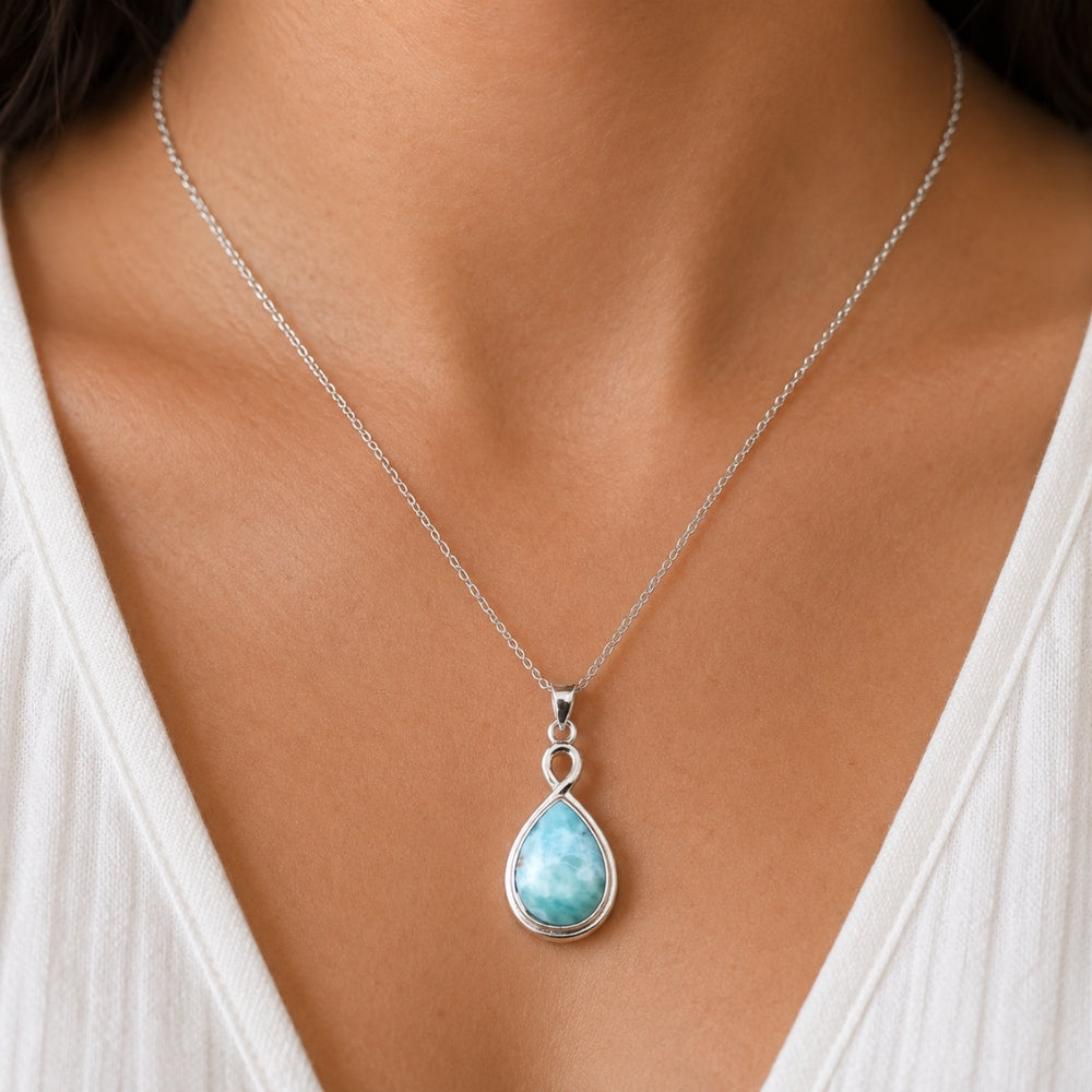 Necklace with a teardrop-shaped pendant featuring a blue gemstone, worn by a person in a white top.