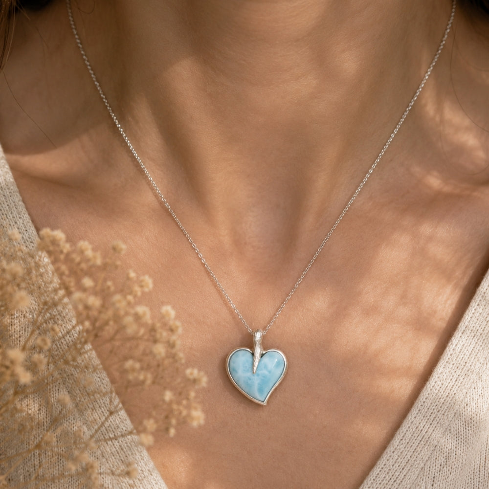 Necklace with a heart-shaped Larimar pendant worn by a person, with a blurred natural background.
