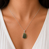 A close-up of a person's neck and chest wearing a silver chain necklace with an irregular, rough-cut green stone pendant.