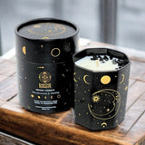 Black candle with celestial design next to its packaging on a wooden surface
