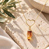 Gold heart necklace with a dangling raw citrine crystal pendant displayed on natural stone in soft sunlight, Earths Elements jewelry.