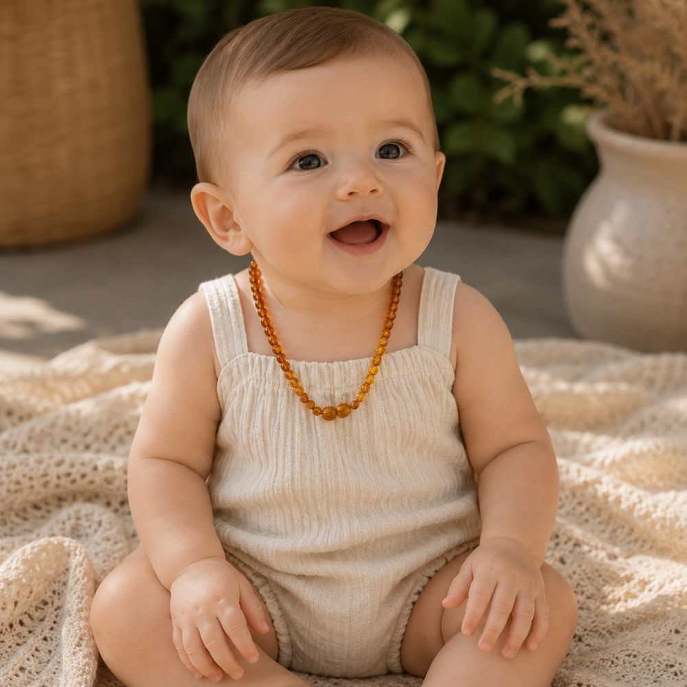 Smiling baby wearing a natural amber teething necklace with polished cognac amber beads in warm, soft natural light.
