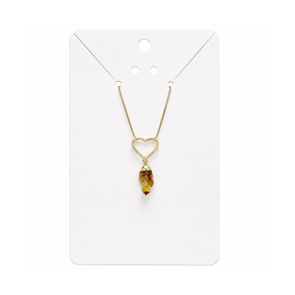 A gold necklace with a heart-shaped pendant and a dangling citrine crystal, displayed on a white card.