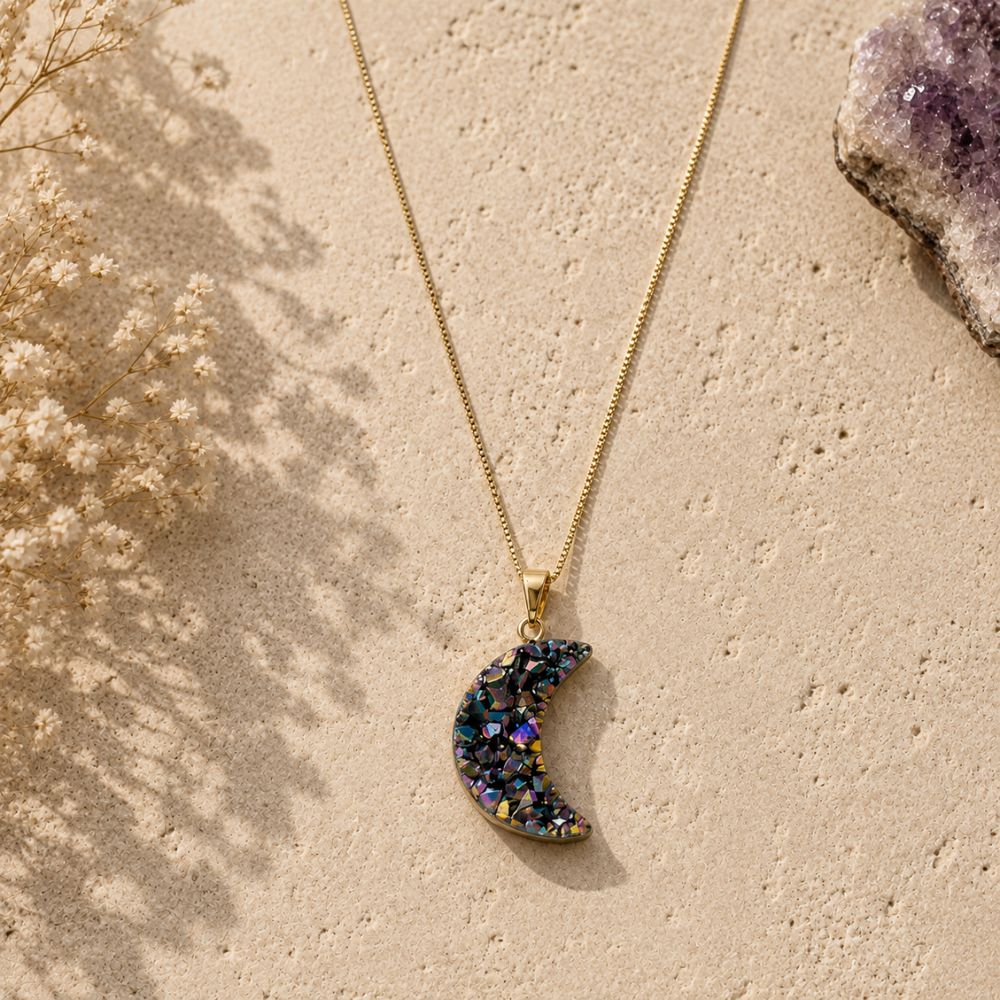Gold chain necklace with a rainbow druzy crescent moon pendant, featuring iridescent crystal details, styled on natural limestone with delicate dried flowers.
