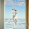 Decorative shell mobile hanging by a window with a view of the ocean.