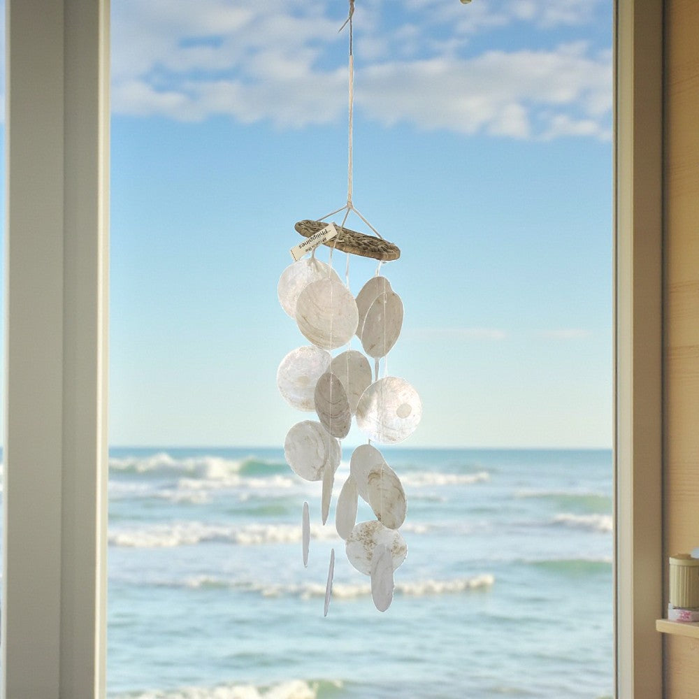 Decorative shell mobile hanging by a window with a view of the ocean.