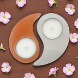 Yin and yang candle holders with candles on a wooden surface surrounded by small pink flowers.