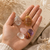 Silver and gold crystal cage pendants displayed with polished crystals on a natural stone surface and soft linen.